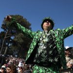 Person in cannabis-themed suit at outdoor gathering.