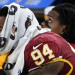 Football player resting on bench with towel.