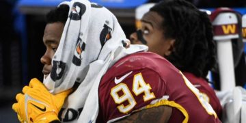 Football player resting on bench with towel.