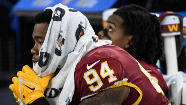 Football player resting on bench with towel.