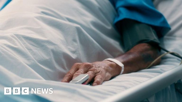 Patient's hand in a hospital bed, wristband visible.