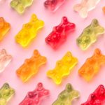 Colorful gummy bears arranged on pink background.