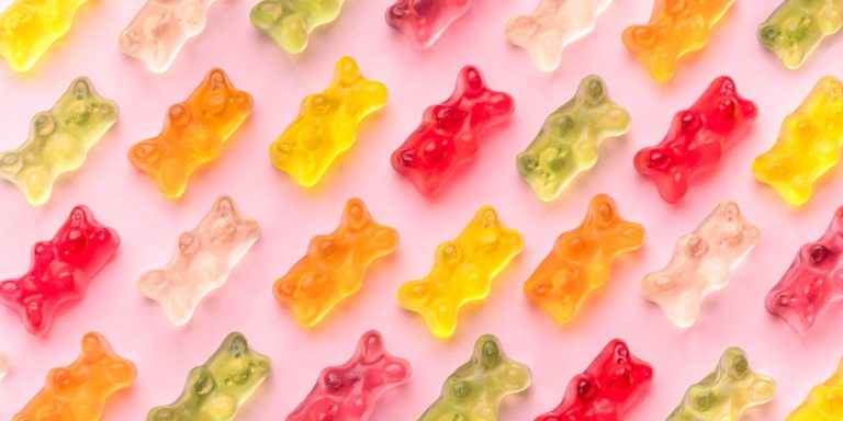 Colorful gummy bears arranged on pink background.