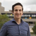 Person smiling outdoors with blurred building background.