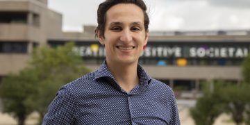 Person smiling outdoors with blurred building background.