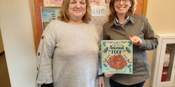 Two people holding animal poop book indoors.