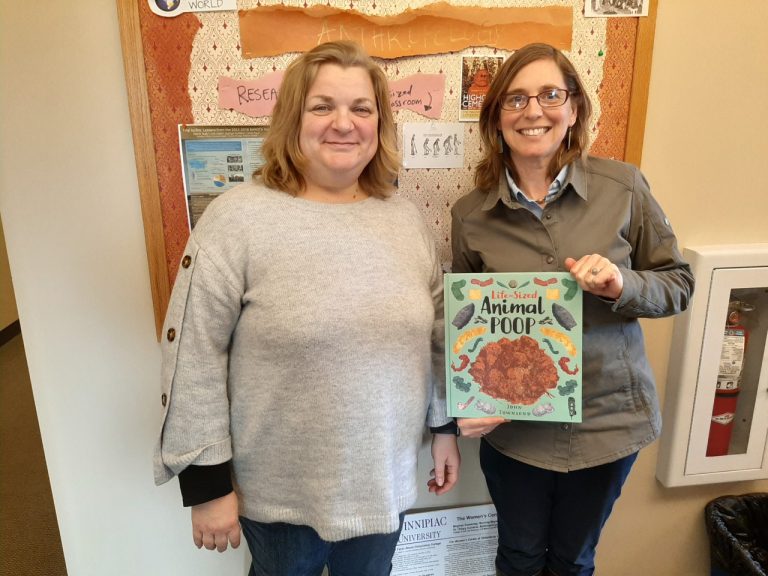 Two people holding animal poop book indoors.