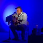 Musician performing acoustic guitar in blue lighting.