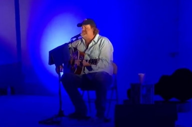 Musician performing acoustic guitar in blue lighting.