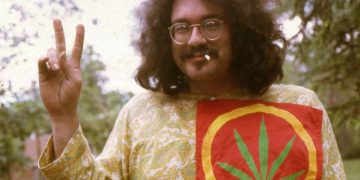 Person holding peace sign with cannabis leaf shirt