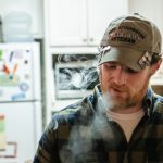 Man in kitchen wearing veteran cap, 2019.