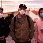 Three masked friends standing outdoors at sunset.