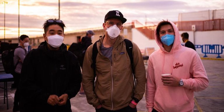 Three masked friends standing outdoors at sunset.