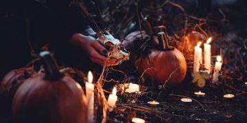 Pumpkins and candles with skull in forest scene.