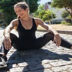 Woman exercising outdoors with speaker and water bottle.