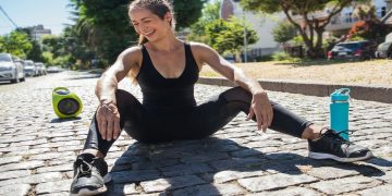 Woman exercising outdoors with speaker and water bottle.