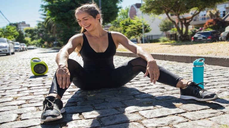 Woman exercising outdoors with speaker and water bottle.