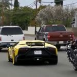 Yellow sports car followed by police motorcycle on street.