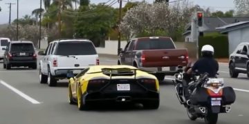 Yellow sports car followed by police motorcycle on street.