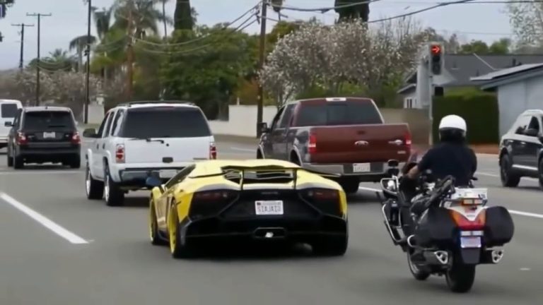 Yellow sports car followed by police motorcycle on street.