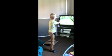 Child playing a tennis video game indoors.