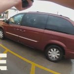 Person pointing camera at red van in parking lot.