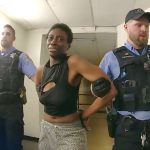 Police officers escorting a handcuffed individual in hallway.