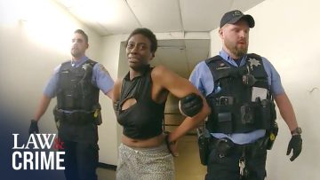 Police officers escorting a handcuffed individual in hallway.