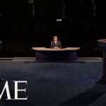 Politicians debate on stage with moderator present.