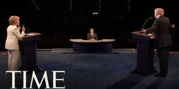 Politicians debate on stage with moderator present.