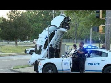 Police car crashed vertical against pole, officers nearby.