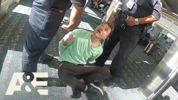 Man in handcuffs with two officers at airport.