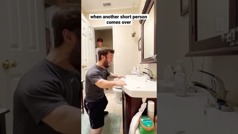 Man kneeling by bathroom sink, another enters room.