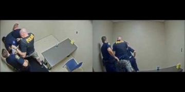 Police officers restraining individual in interrogation room.