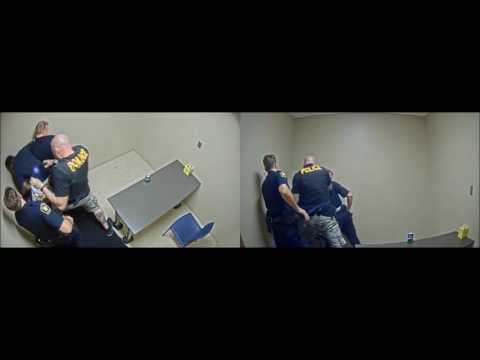 Police officers restraining individual in interrogation room.