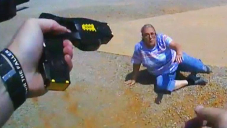 Taser aimed at woman on ground.