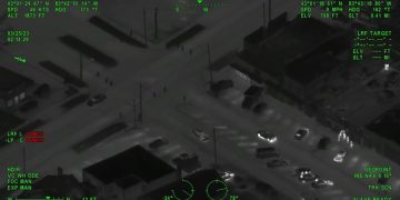 Aerial night vision of city intersection with vehicles.