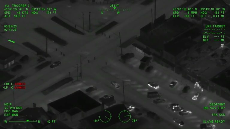 Aerial night vision of city intersection with vehicles.