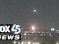 Nighttime cityscape with bright lights and news logo.