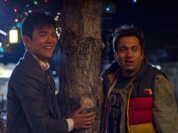 Two people standing by a decorated tree at night.