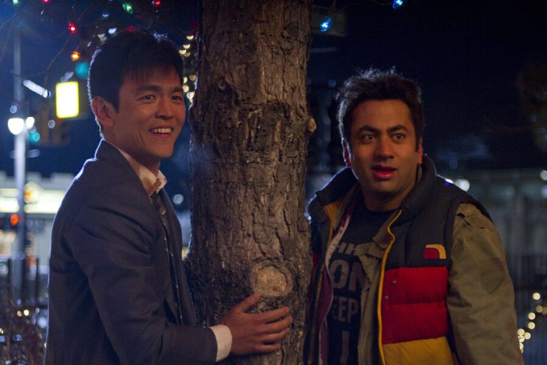 Two people standing by a decorated tree at night.