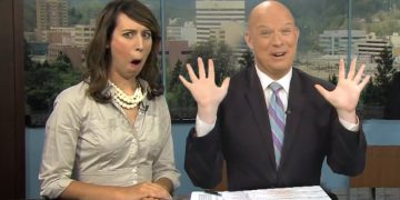 Two amused TV anchors at news desk.