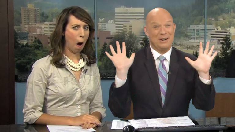 Two amused TV anchors at news desk.