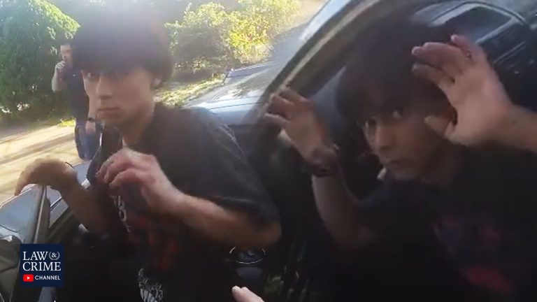 Two young men in car with raised hands.