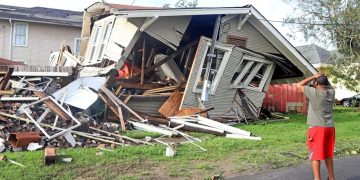 Man observing house destroyed by hurricane damage.