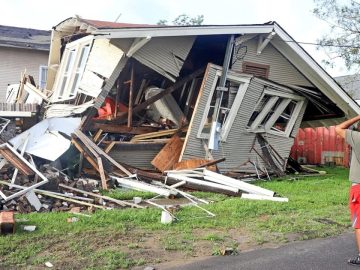 Man observing house destroyed by hurricane damage.