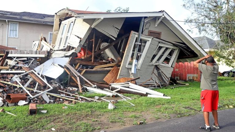 Man observing house destroyed by hurricane damage.