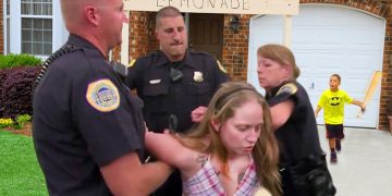 Woman arrested near lemonade stand, child in background.