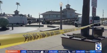 Police tape blocking pier entrance with vehicles nearby.