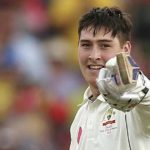 Cricketer smiling and pointing with a glove.